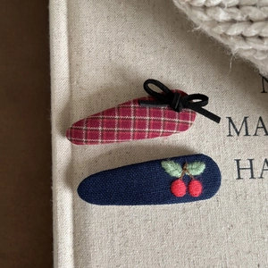 Close-up of fabric hair clips featuring red gingham bow and navy cherry embroidery details