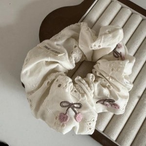 Dettaglio scrunchie in pizzo crema con ricamo a ciliegia ed etichetta tessuta