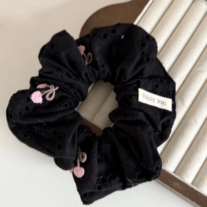 Dettaglio di un elastico in pizzo nero con ricamo a ciliegia rosa ed etichetta del marchio