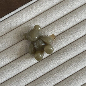 Vue macro d'une pince à cheveux ours vert olive avec texture marbrée sur un plateau beige