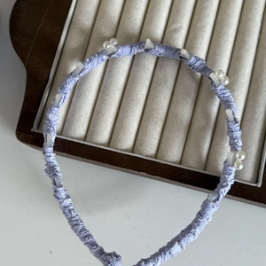 Dettaglio del cerchietto in tessuto viola lavanda con perle bianche e ciondoli chiari