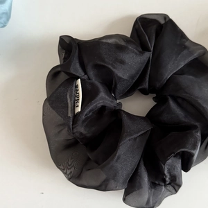 Detail of a large black sheer organza hair scrunchie with soft pleated texture and label