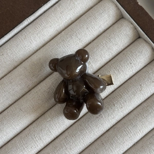 Détail de la pince à cheveux ours brun foncé avec fermoir en métal doré sur tissu