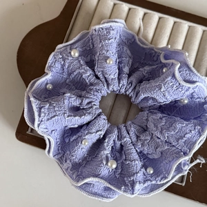 Dettaglio dell'elastico scrunchie in crepe viola con perle bianche e bordo a onde