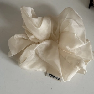 Detail of a large cream-colored silk scrunchie featuring elegant soft fabric folds
