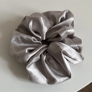 Macro shot of silver-grey satin fabric scrunchie with smooth silk texture and soft shine