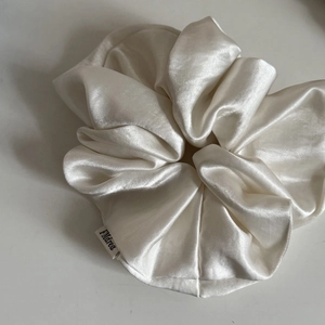 Detail of the white satin scrunchie showing glossy texture and a Fmdrea brand label
