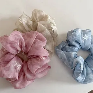 Detailansicht von Chiffon-Haargummis mit weißen Blumenstickereien in zarten Pastellfarben