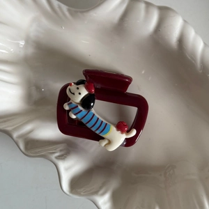 Detail van een bordeaux haarclip met cartoon teckel op een schaal met schelpentextuur