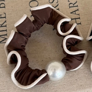Detail of a dark brown pleated scrunchie with white trim and a large elegant pearl bead
