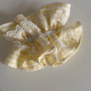 Detailed view of yellow plaid scrunchie with delicate white lace trim and elastic ruffles