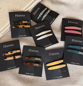 Close-up of elegant acetate hair clips with gold lettering on a beige textured background