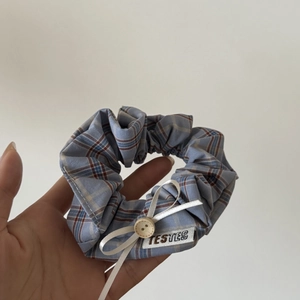 Close-up of blue plaid scrunchie featuring white ribbon bow and rustic wooden button