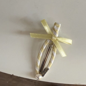 Detail of yellow striped ribbon hair clip with bow, pearl, and engraved metal clasp