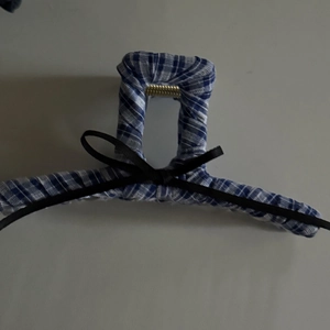 Detail view of a blue plaid fabric hair claw clip with a black ribbon bow and metal spring