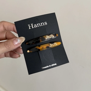 Detailed view of tortoiseshell leaf hair clips on black display card held by hand