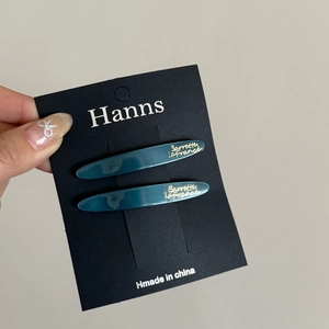 Macro detail of teal acetate leaf hair clips with gold lettering on display card