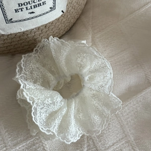 Detail of white handmade layered lace scrunchie with vintage embroidery on woven texture