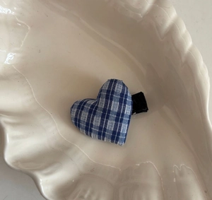 Detailed view of blue gingham heart hair clip resting on a white ceramic shell tray