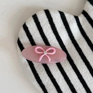 Vue détaillée d'une barrette ovale rose avec noeud et strass sur fond rayé moderne