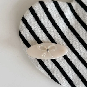 Détail d'une barrette ovale en acétate avec un nœud pailleté et un strass brillant de qualité