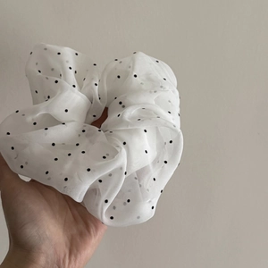 Close-up of creamy white chiffon scrunchie with black polka dots and layered texture