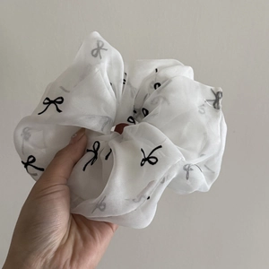 Elegant white tulle scrunchie with black bow pattern held in hand for a soft, minimalist look