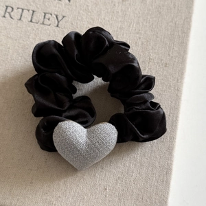 Silk satin black scrunchie with grey fabric heart pendant on a neutral linen background