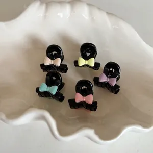 Cinq mini pinces à cheveux noires avec nœuds pastel sur un plateau en coquillage