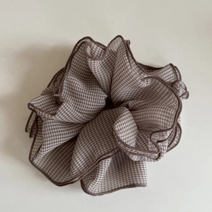 Detail eines kaffee-weiß karierten Scrunchie mit feinen Overlock-Kanten und weichem Stoff