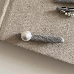 Macro view of grey tweed fabric hair clip with a white pearl on a linen background