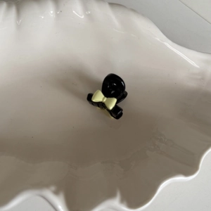 Mini pince à cheveux noire avec un joli nœud jaune sur un plateau blanc