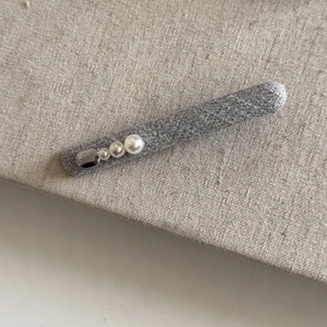 Detailed close-up of dark grey fabric hair clips with white pearls and silver accents