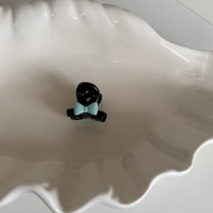 Mini pince à cheveux noire avec un nœud bleu clair sur un plateau en coquillage