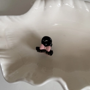 Mini pince à cheveux noire avec nœud rose sur un plat en céramique ondulé blanc