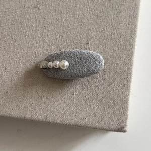 Close-up of a grey fabric oval hair clip decorated with four white gradient pearls and silver metal