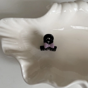 Vue détaillée d'une mini pince à cheveux noire ornée d'un petit nœud violet sur une assiette