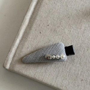 Close-up of grey fabric hair clip with white pearls and silver metal bead on linen