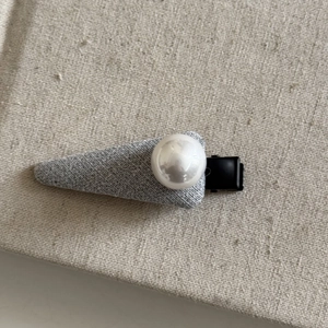 Detail of grey fabric hair clip with a centered white pearl and black metal clip