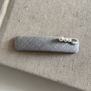 Detail view of gray textured fabric hair clip with three elegant white pearls and a stone