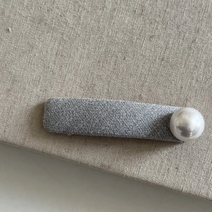 Close-up of a gray textured fabric hair clip with a large white pearl accent