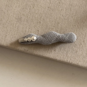 Detail of grey wavy fabric hair clip with three white pearls on linen background