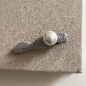 Detailed macro view of gray fabric texture and lustrous pearl on a stylish hair clip