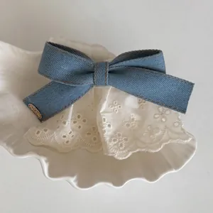 Denim bow hair clip with white lace trim and metal tag in a decorative shell dish