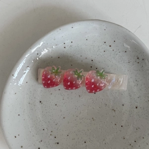 Détail d'une pince à cheveux fraise avec fruits pailletés sur une base nacrée
