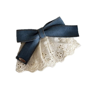 Denim bow hair clip with lace trim and vintage metal tag on white background
