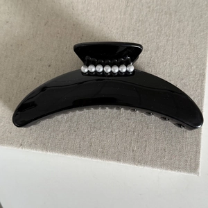 Gros plan d'une pince à cheveux noire brillante ornée de sept perles sur tissu gris