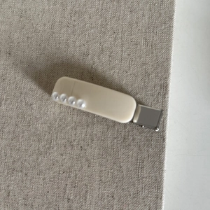 Gros plan d'une pince à cheveux en acrylique blanc crème avec quatre perles sur lin