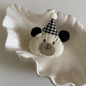 Vue détaillée d'une barrette à cheveux ours en peluche avec chapeau vichy sur un plat blanc
