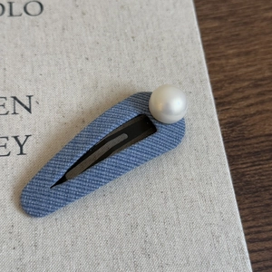 Detailed macro view of denim blue fabric hair clip with a large white round pearl embellishment